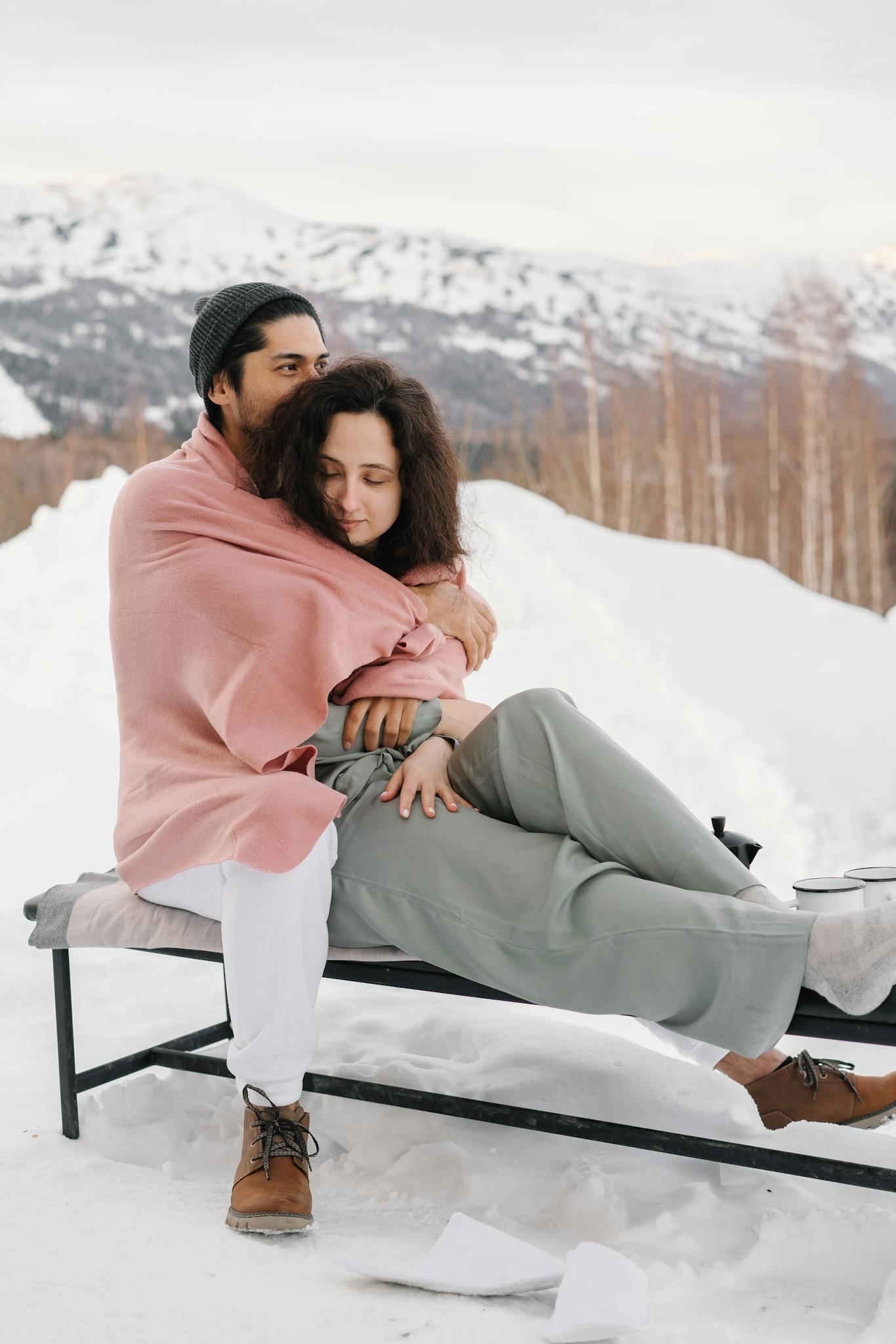 A loving couple embraces outdoors in a serene snowy winter setting, exuding warmth and togetherness.